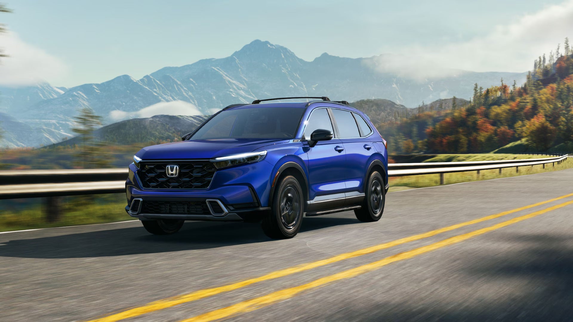 a blue 2025 honda cr-v hybrid driving on a paved road in the mountains with a guard rail next to the road