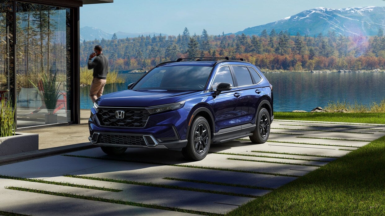 a blue 2025 honda cr-v hybrid parked nex to a house on the lake with mountains in the background