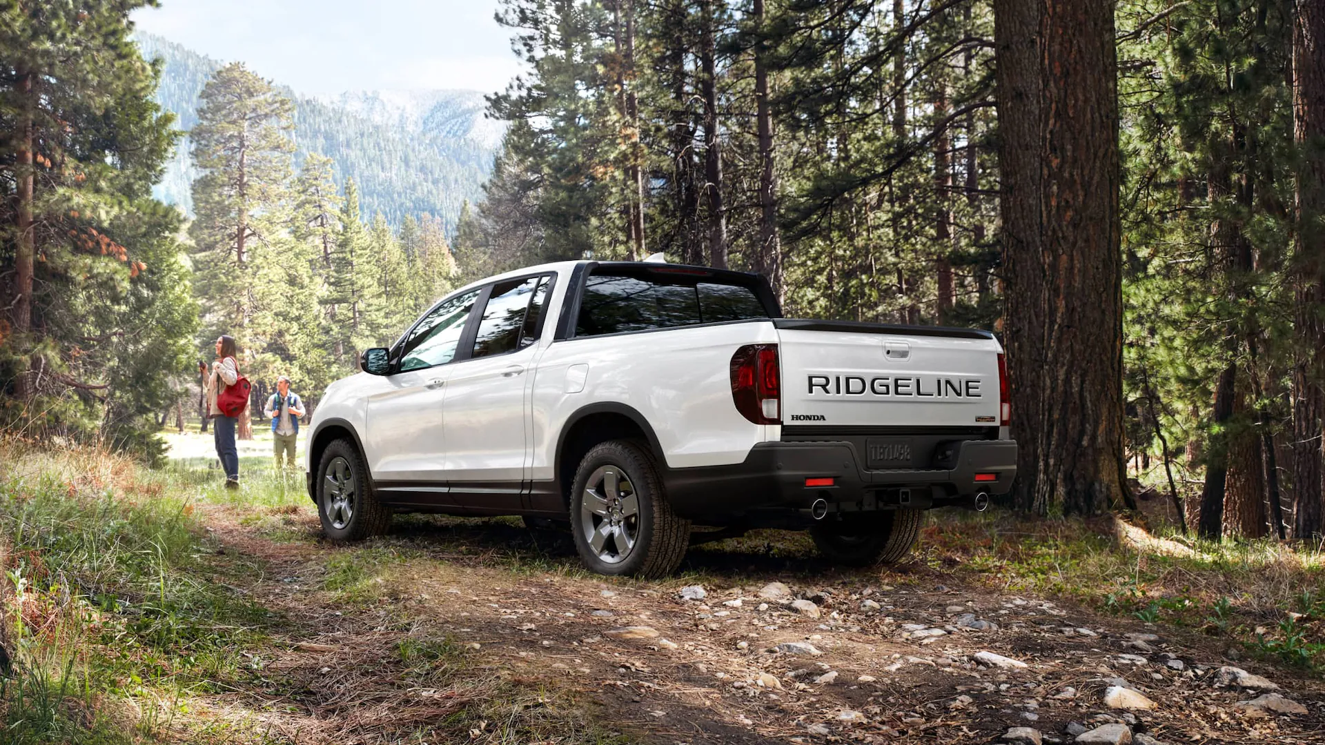 2025 Honda Ridgeline truck hauling a trailer with UTVs on a dirt path in a desert terrain.