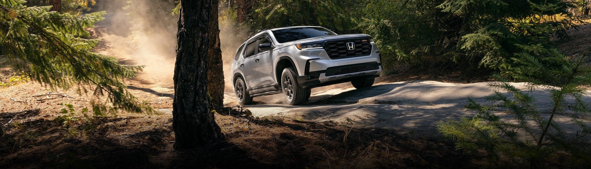 a white 2025 Honda Pilot driving on a dirt trail