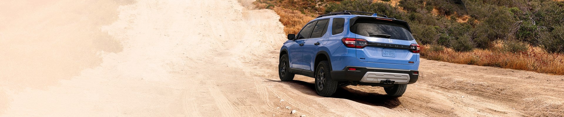 a white 2025 Honda Pilot driving on a dirt trail